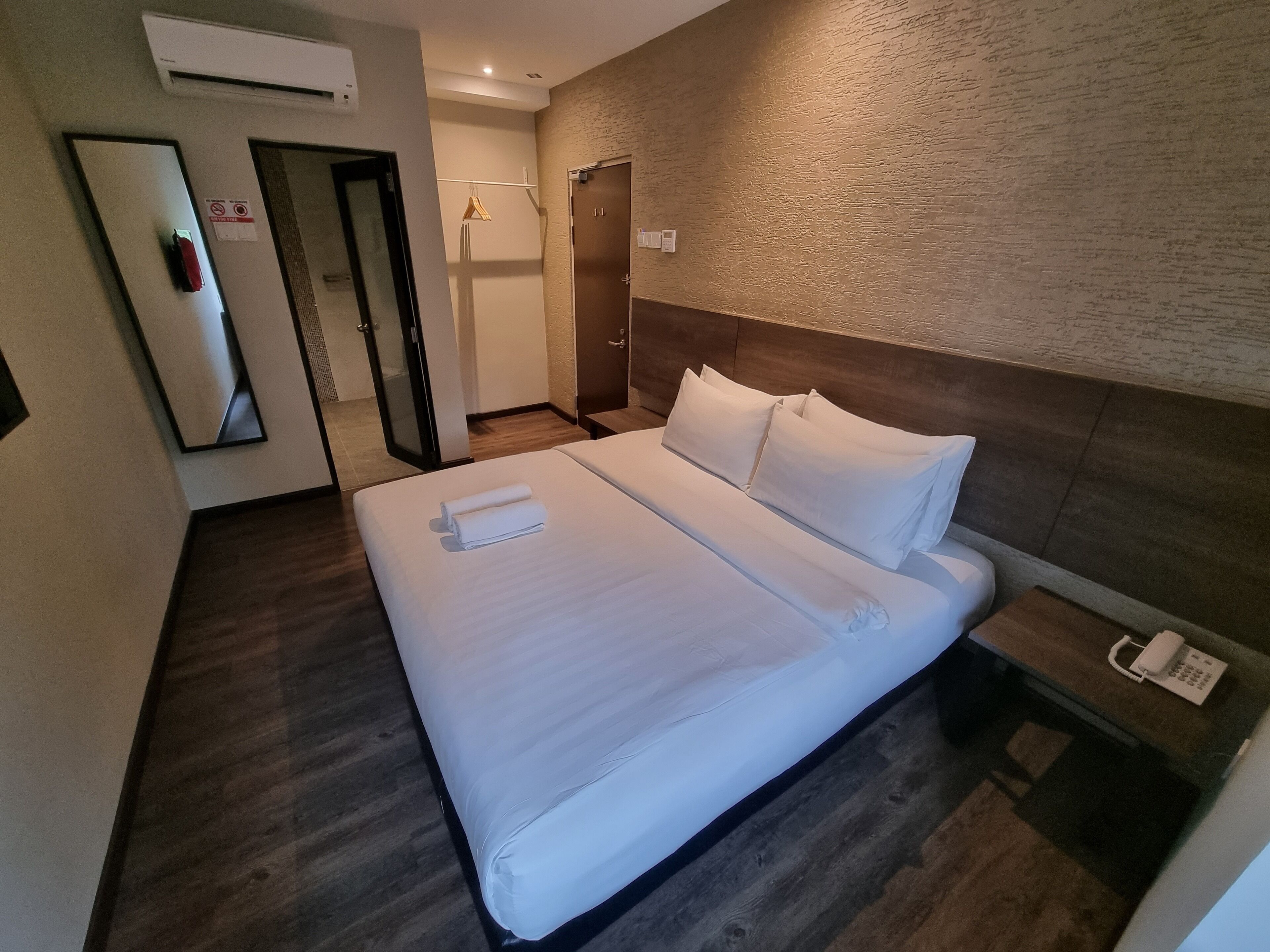 A hotel room with a large bed, a wooden headboard, a bedside telephone, and a mirror on the wall.
