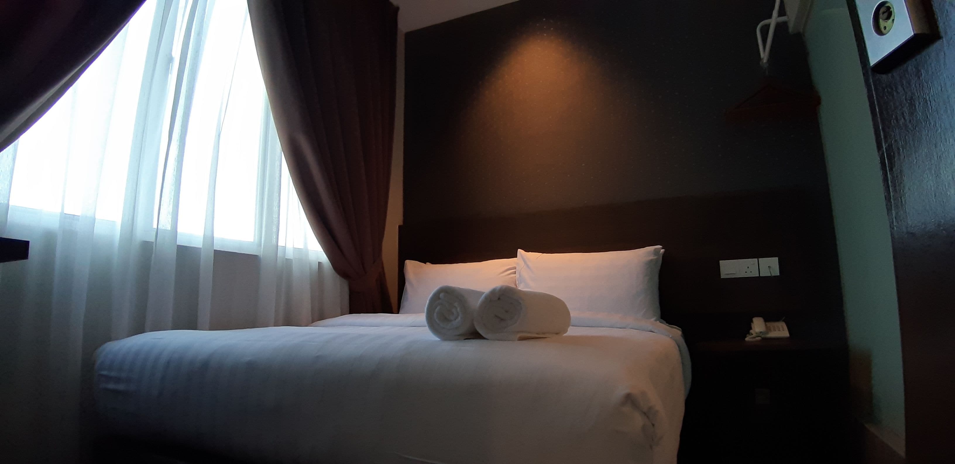 Une chambre d’hôtel avec un lit bien fait, une table de chevet avec un téléphone et une fenêtre avec des rideaux.