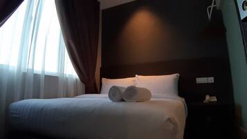 Una habitación de hotel con una cama bien hecha, una mesita de noche con un teléfono y una ventana con cortinas.