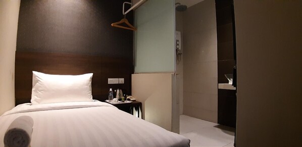 A hotel room with a bed, bedside table, and a hanging coat rack.
