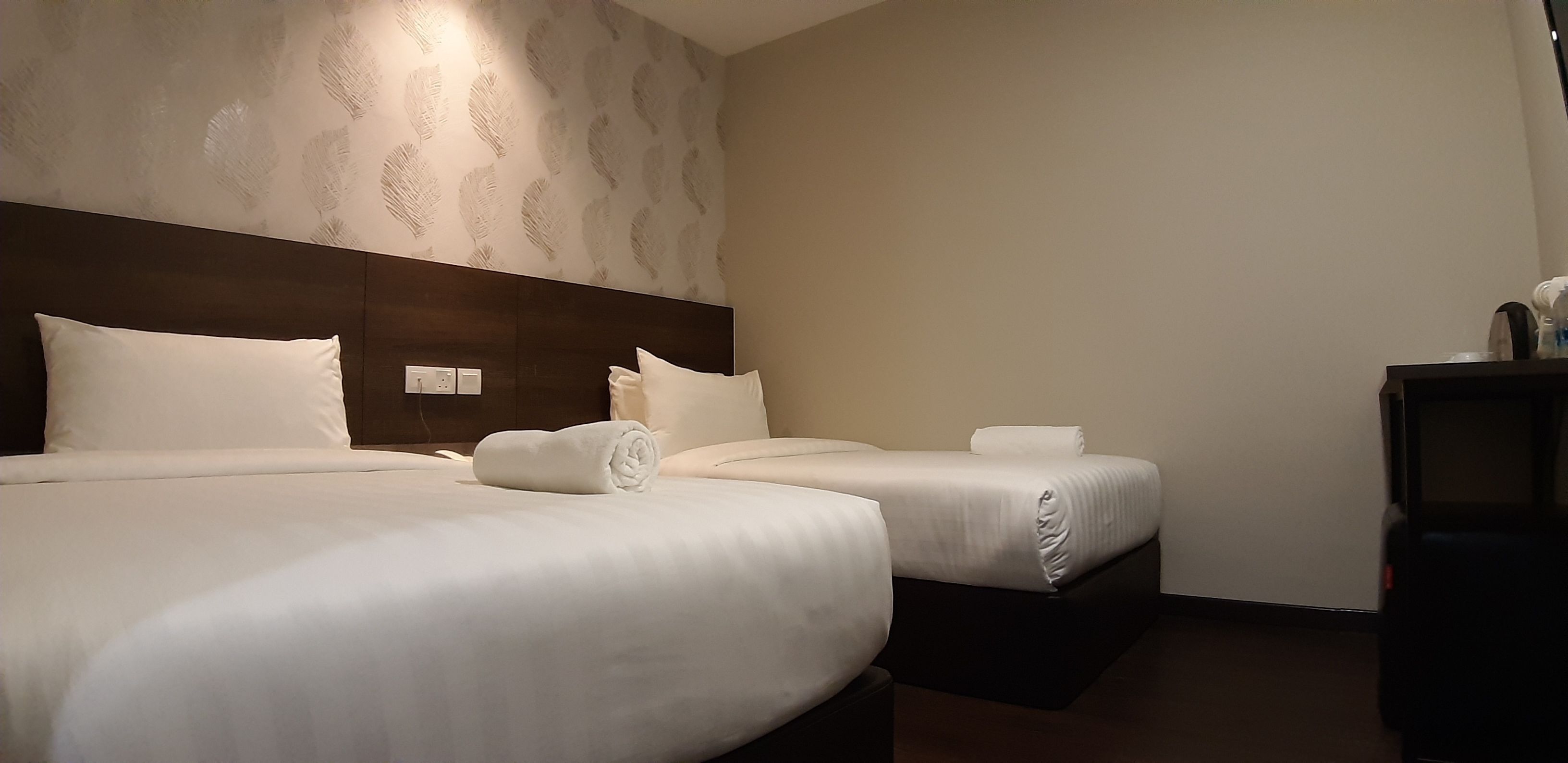 Una habitación de hotel con dos camas, un cabecero oscuro y un pequeño escritorio con una lámpara.