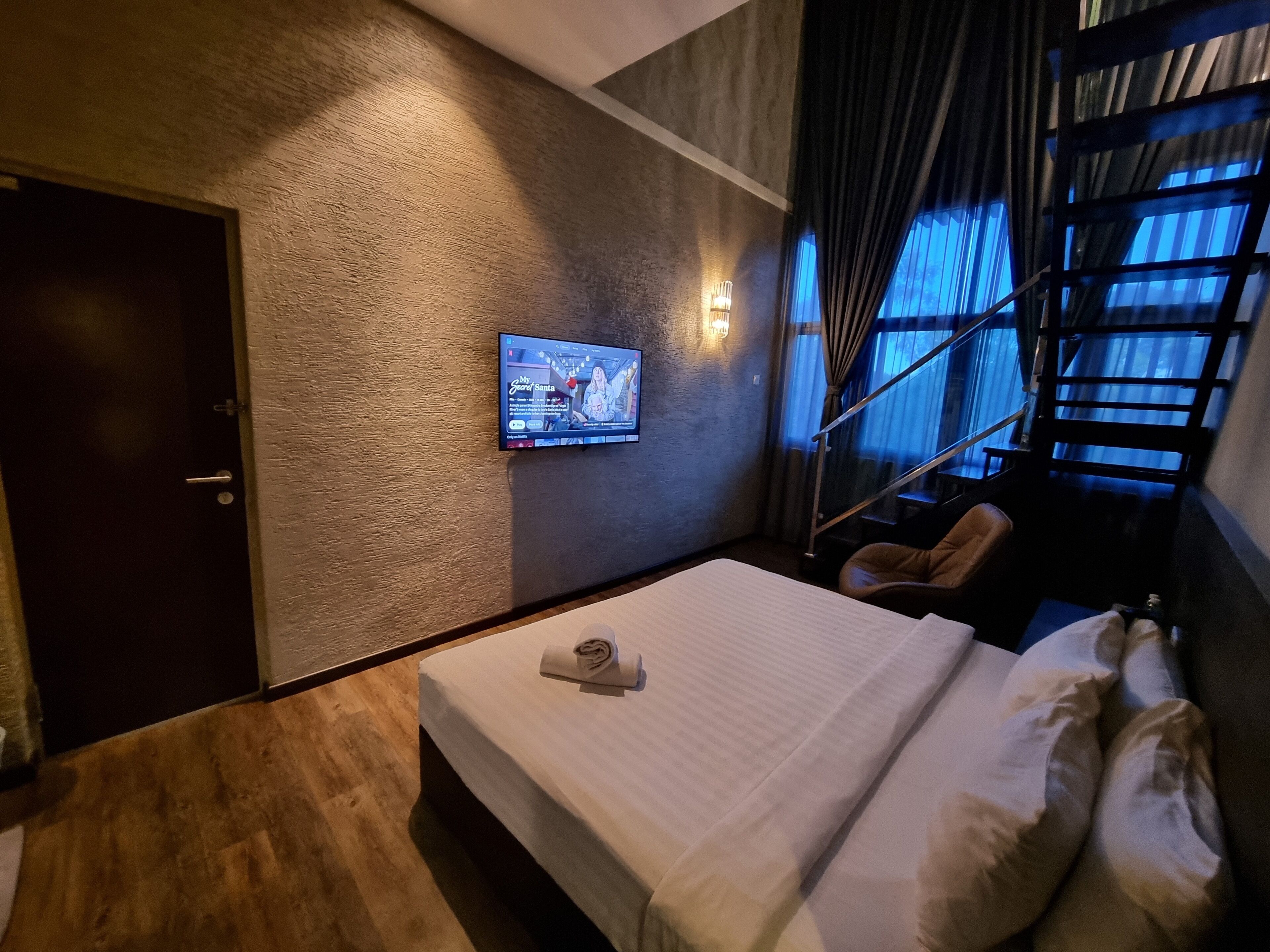 A hotel room with a bed, a TV mounted on the wall, a door, and a staircase.