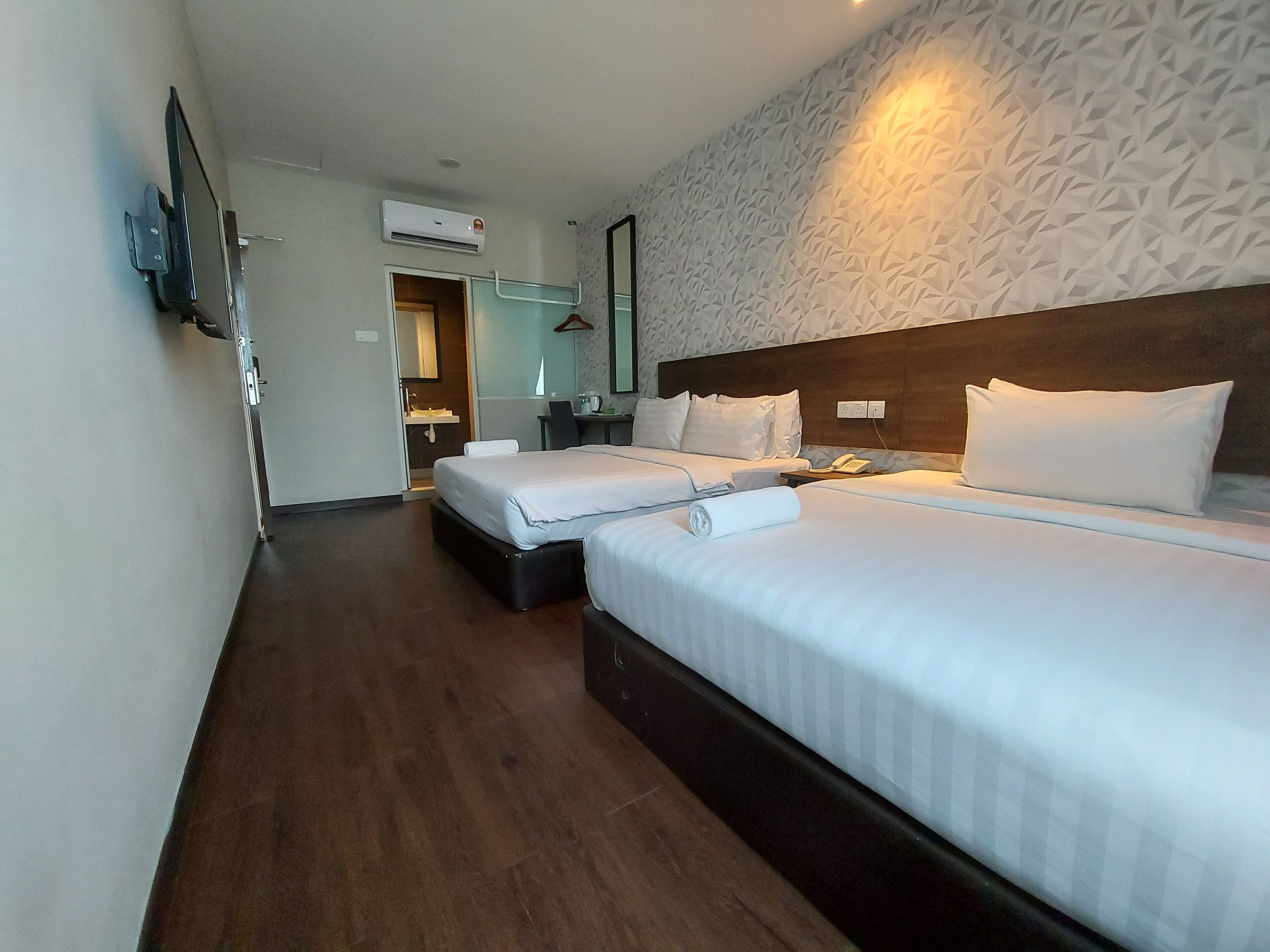 Une chambre d’hôtel avec deux lits, un bureau, une chaise, un miroir et un téléviseur fixé au mur.