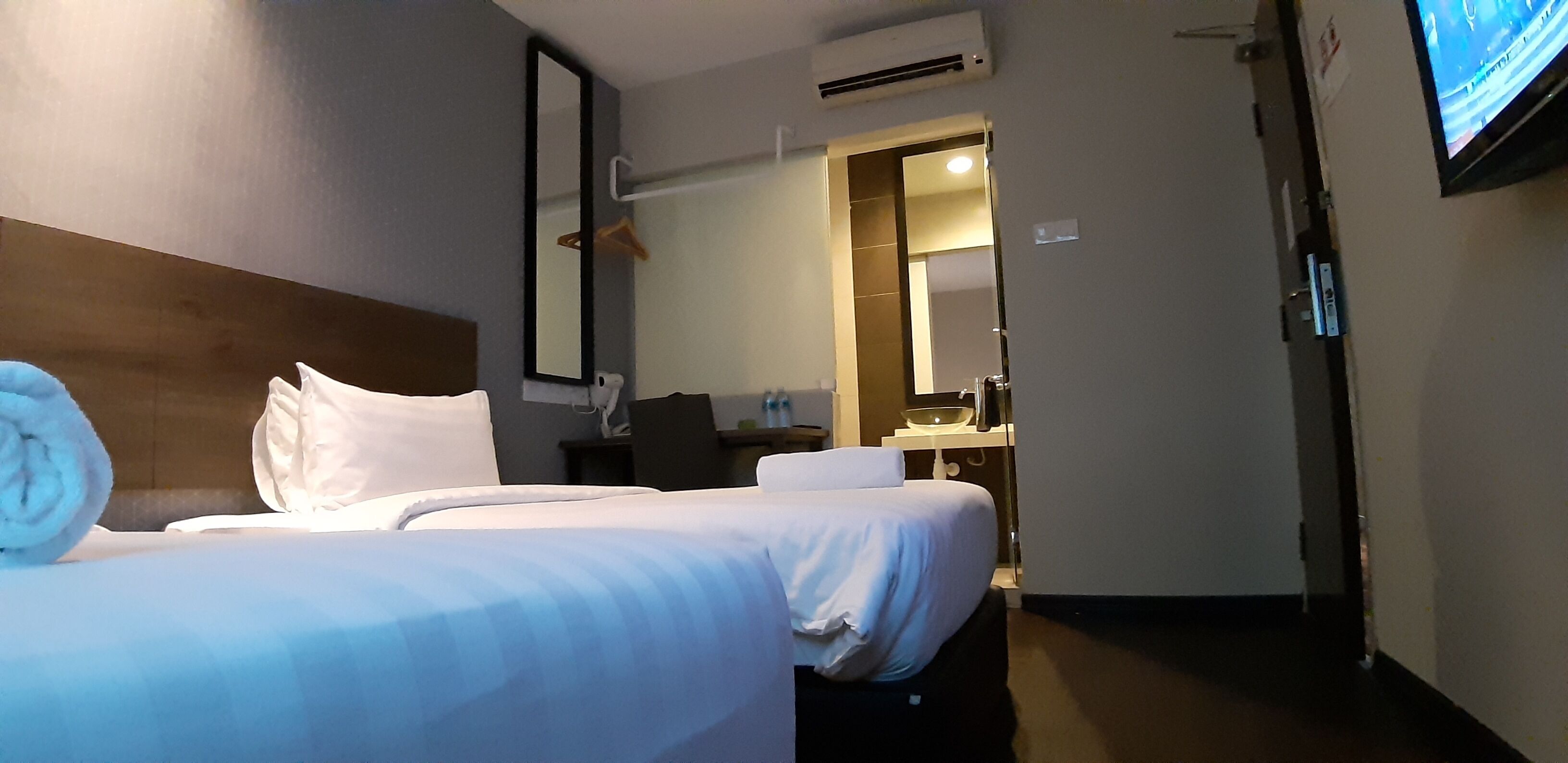 Ein Hotelzimmer mit Bett, Fernseher, Spiegel und einem durchgegangenen Tür sichtbaren Badezimmer.