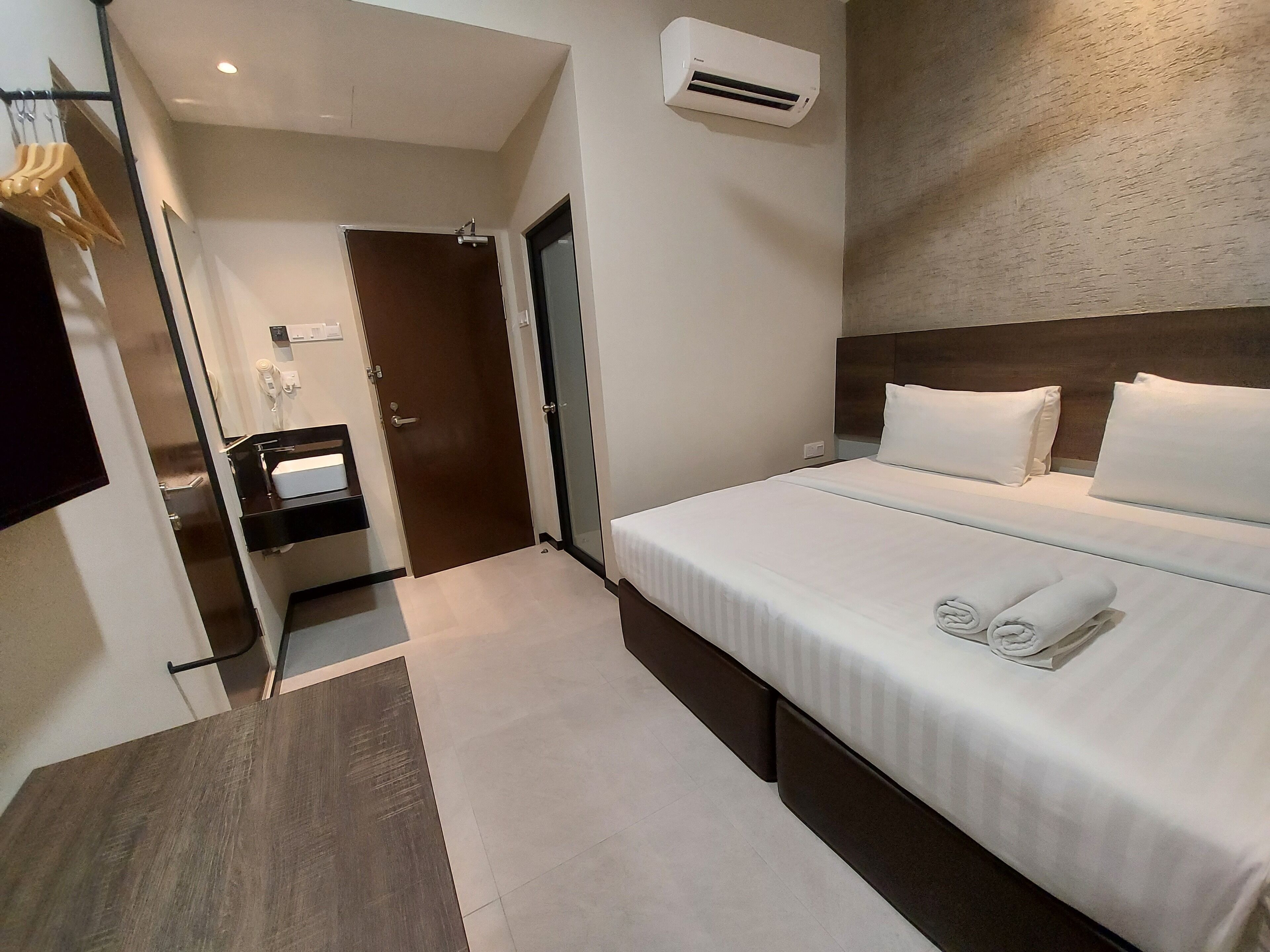 Una habitación de hotel moderna con una cama bien hecha, una mesita de noche pequeña y un aire acondicionado instalado en la pared.