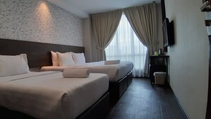 Quarto de hotel com duas camas, televisão, uma pequena mesa e janela com cortinas.