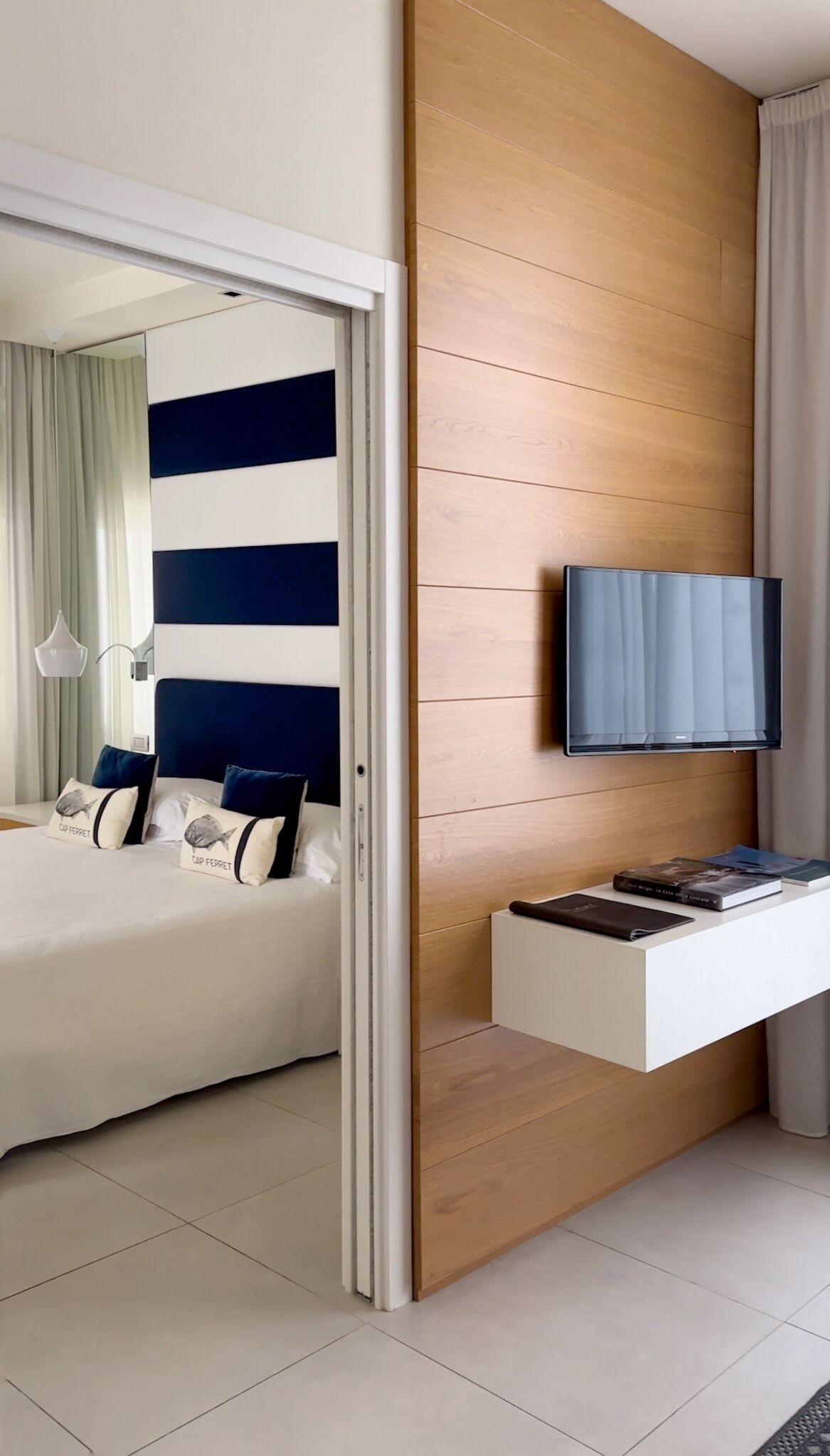 Ett modernt hotellrum med en säng, en tv som är monterad på en väggpanel i trä och ett skrivbord med en bok och ett anteckningsblock.