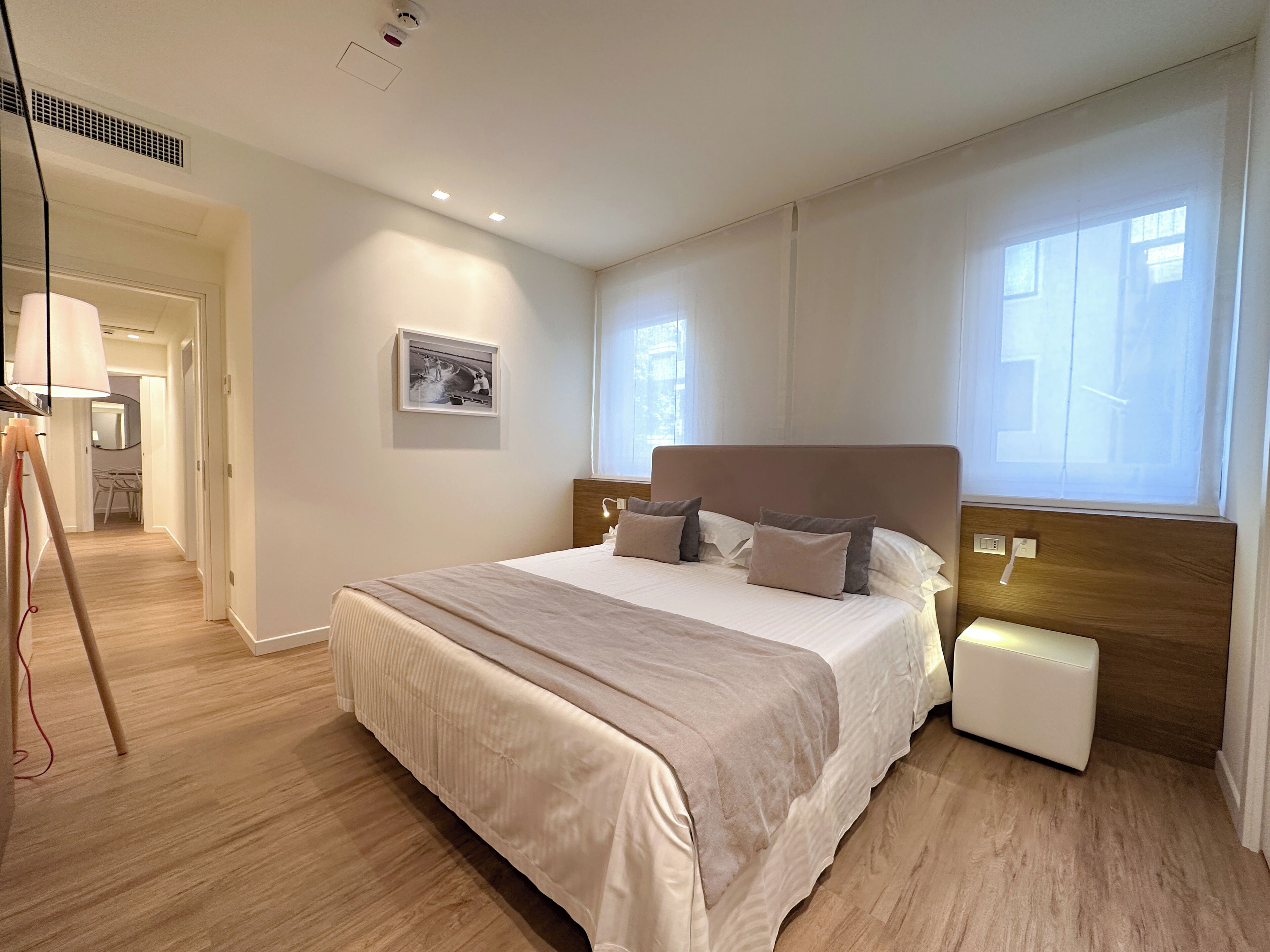 Un dormitorio moderno con una cama grande, una mesita de noche, un cuadro enmarcado en la pared y una ventana que deja entrar luz natural.