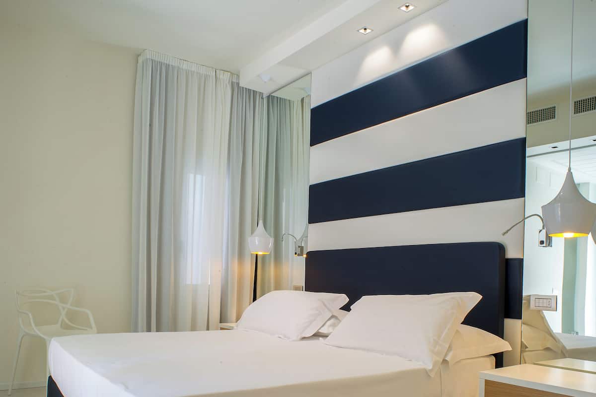 A modern hotel room with a large bed, a bedside table, a mirror, and a window with curtains.