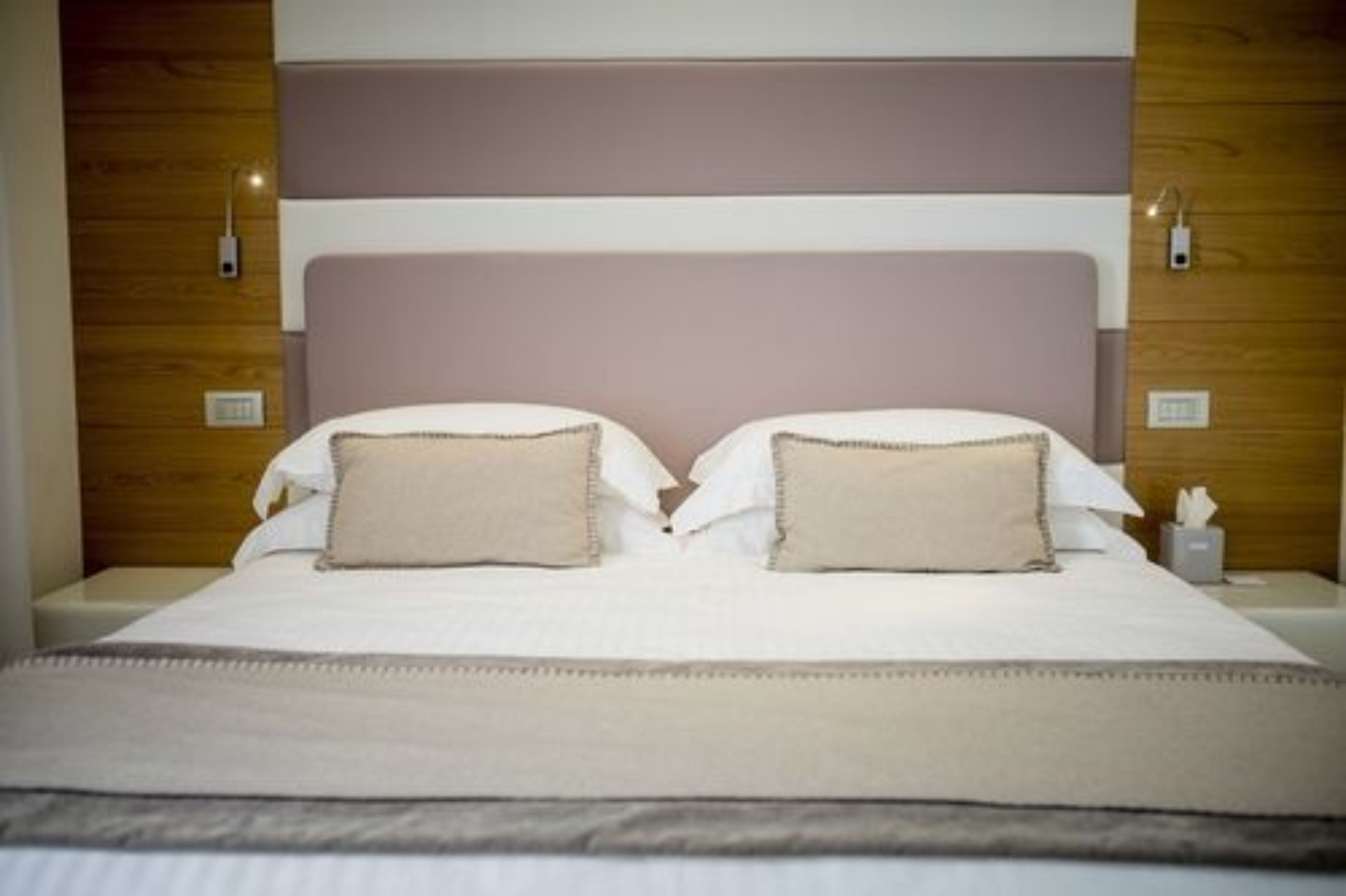 A neatly made bed with a headboard, two pillows, and a bedside table with a tissue box.