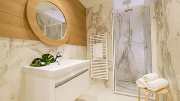 A modern bathroom with a marble vanity, a wooden-framed mirror, a glass shower enclosure, and a towel stand.