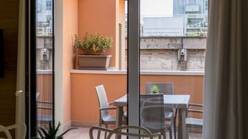 A dining area with a wooden table and chairs, a potted plant, and a view of the outside balcony.