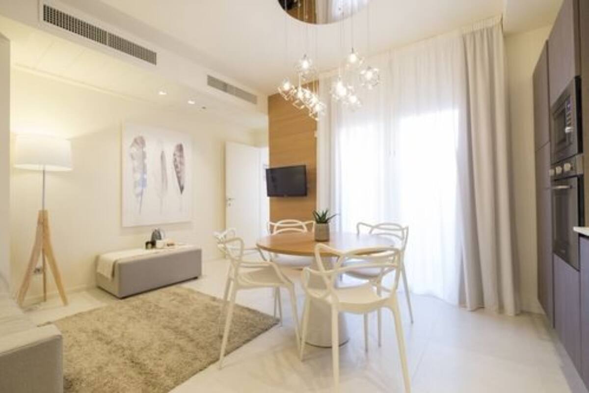 A modern dining area with a round table, white chairs, a wooden bench, and a chandelier.