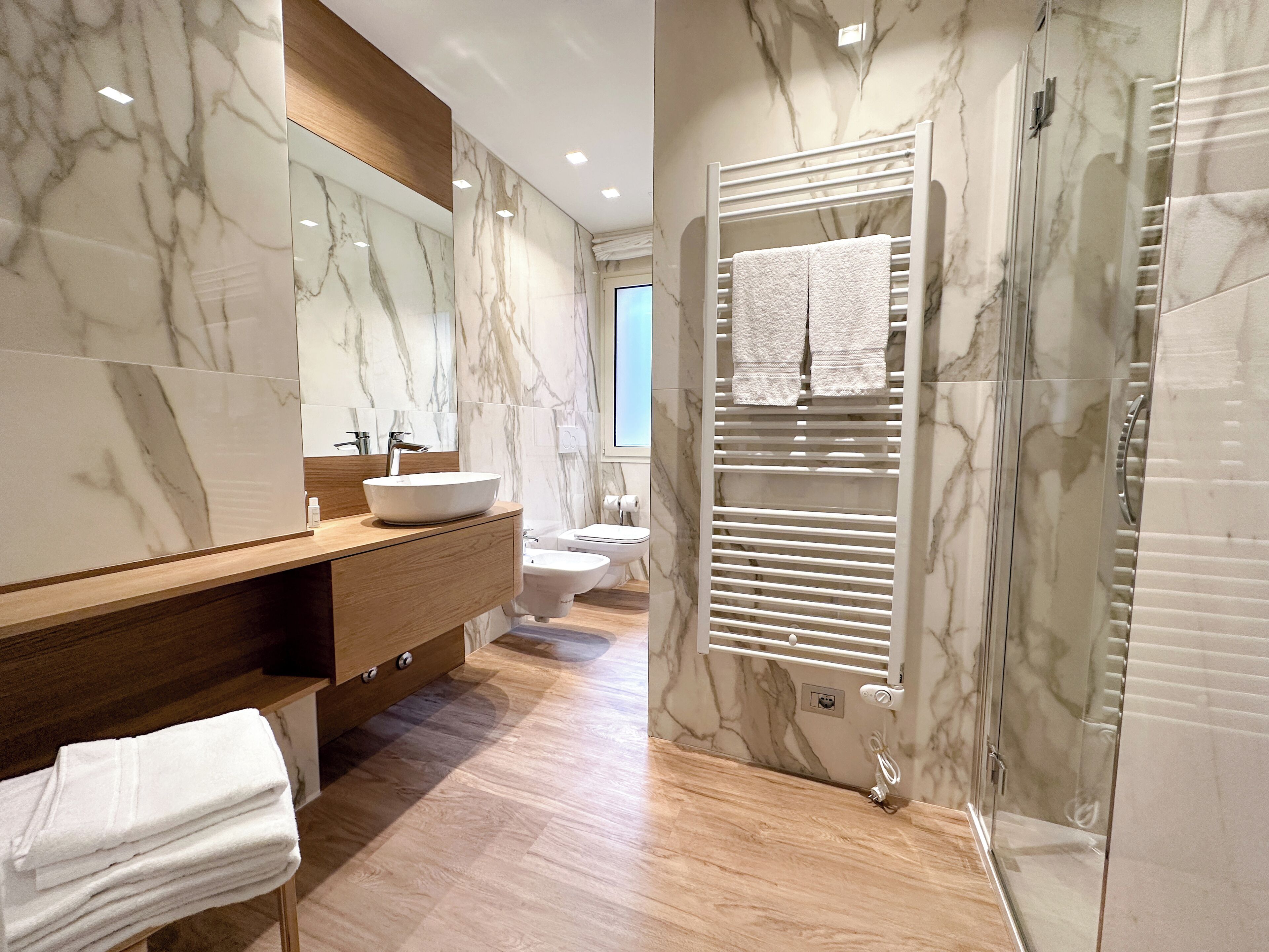 A modern bathroom with a marble vanity, a sink, a toilet, and a shower area.