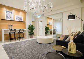 A modern hotel lobby with a reception desk, bar stools, a round seating area, and a sofa with a vase of reed sticks.