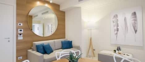 Una sala moderna con una mesa redonda de madera, un sofá con cojines azules, un espejo redondo y una lámpara de pie.