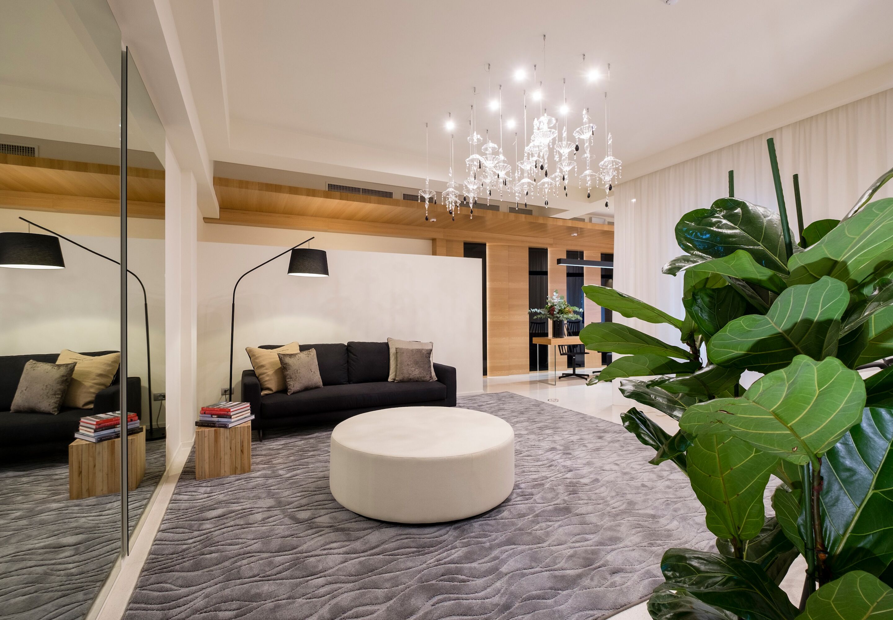 Un salon moderne avec un pouf rond blanc, un canapé noir et un grand miroir.