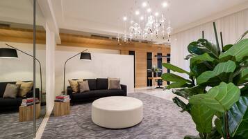 Un salon moderne avec un pouf rond blanc, un canapé noir et un grand miroir.