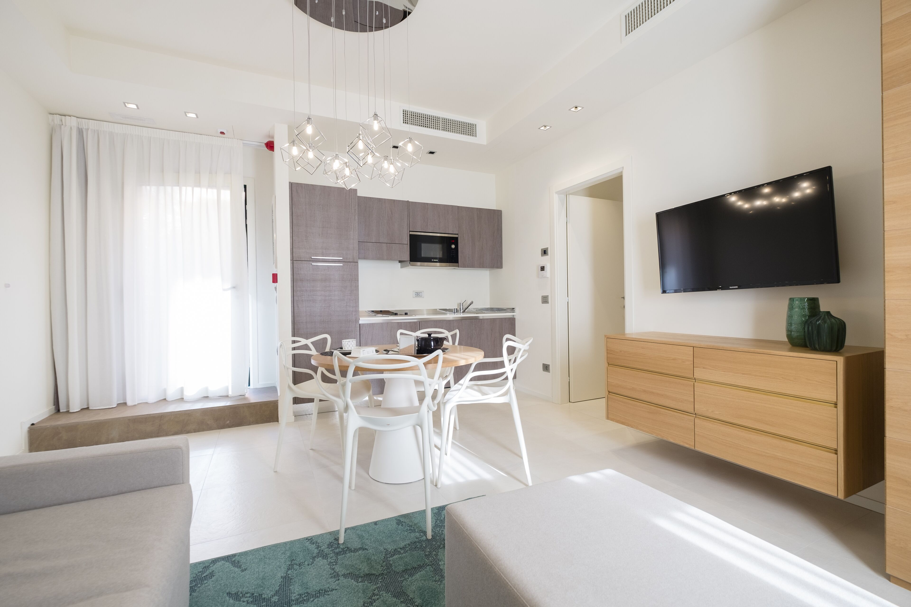 Una sala de estar moderna con comedor, cocina y televisor montado en la pared.