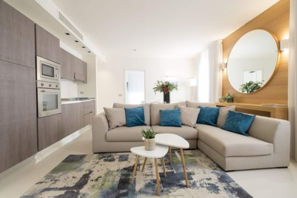 A modern living room with a beige sofa, a small white table, and a large round mirror.
