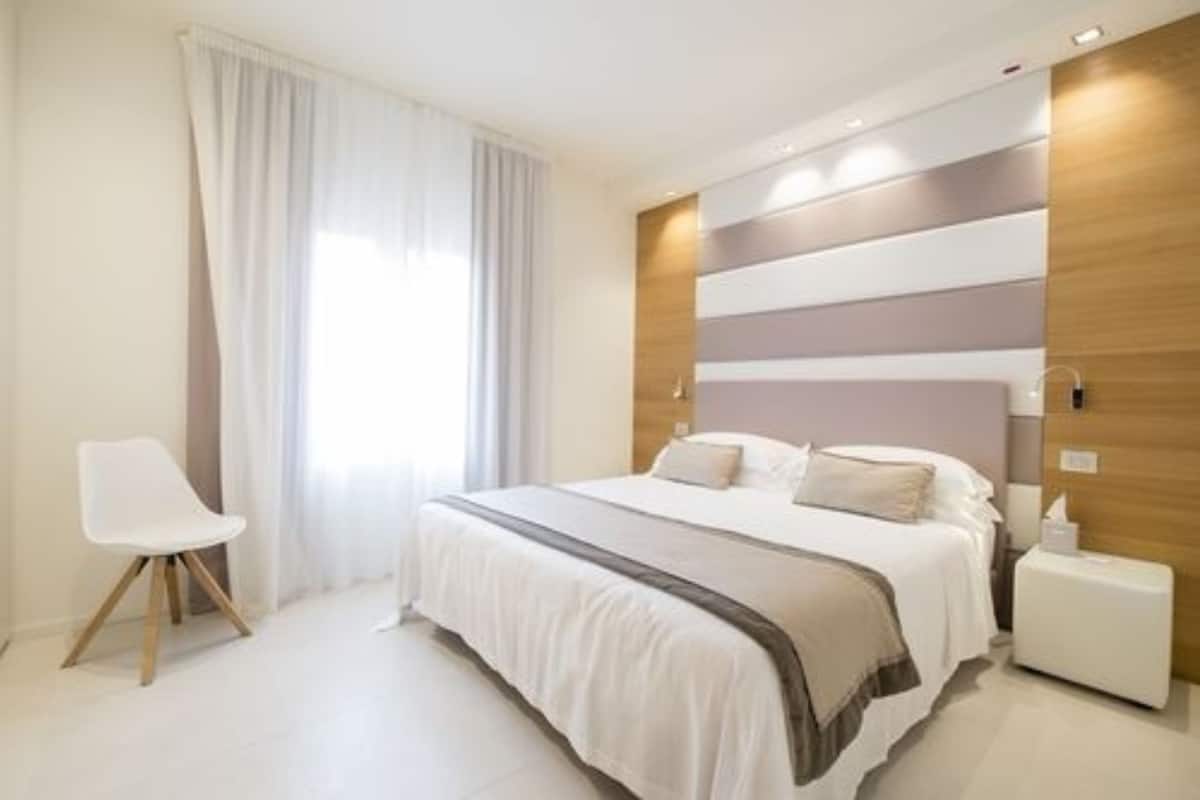 A modern bedroom with a large bed, a bedside table, a chair, and a window with curtains.