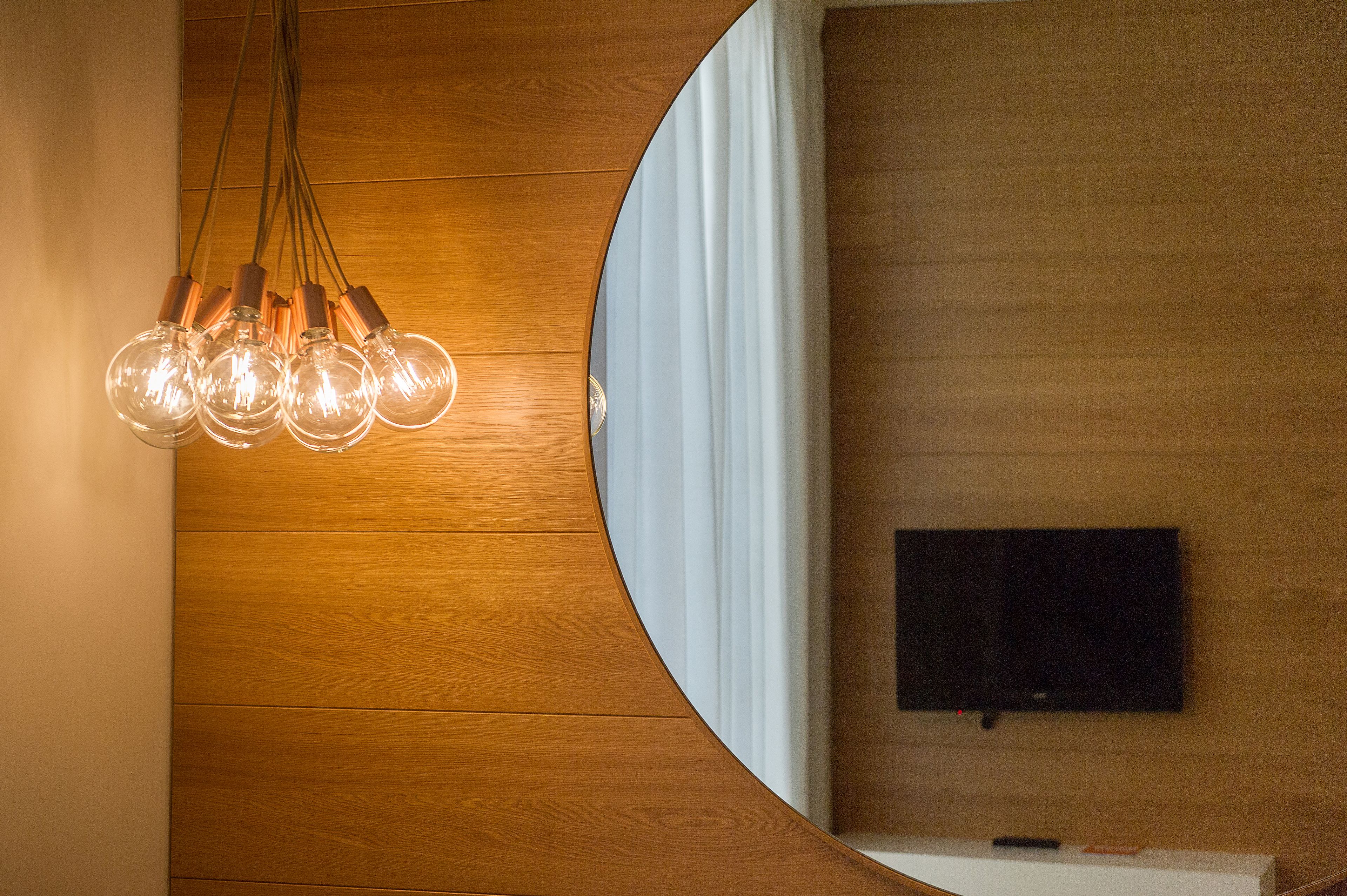 Um interior moderno com parede de madeira, divisória branca curva e luminária pendente com várias lâmpadas.