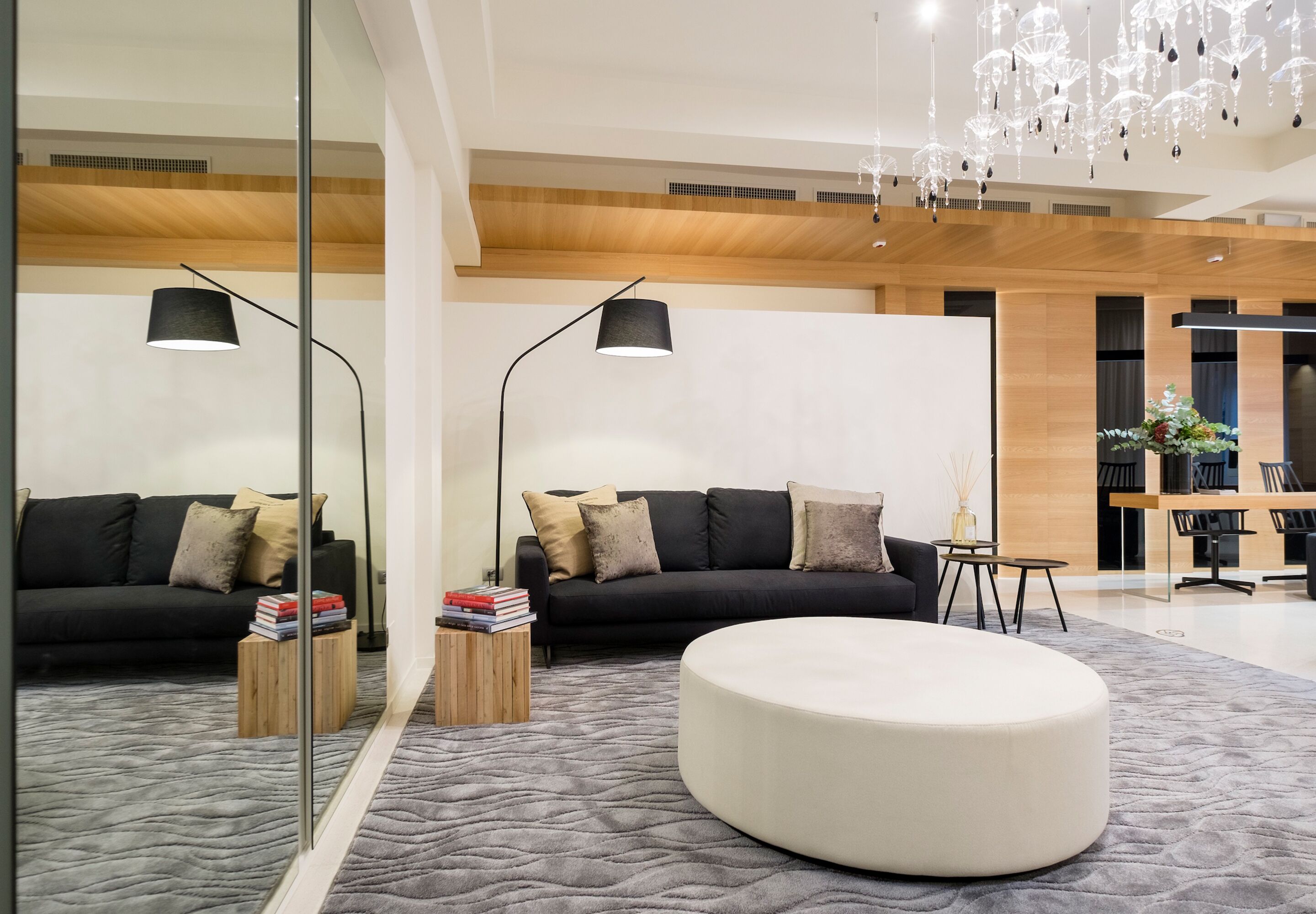 Un salon moderne avec un canapé noir, un pouf rond blanc, une table basse et un miroir qui reflète la pièce.