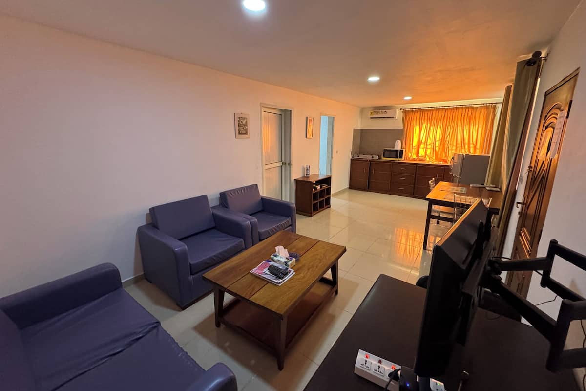 A living room with a sofa set, a coffee table, a TV, and a kitchen area with a microwave.