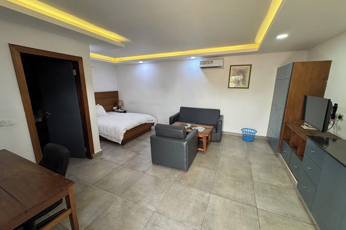 A hotel room with a bed, a sofa, a small table, a TV, and a desk.