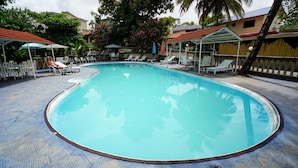 Una piscina con sillones de descanso y sombrillas, rodeada de árboles y edificios.