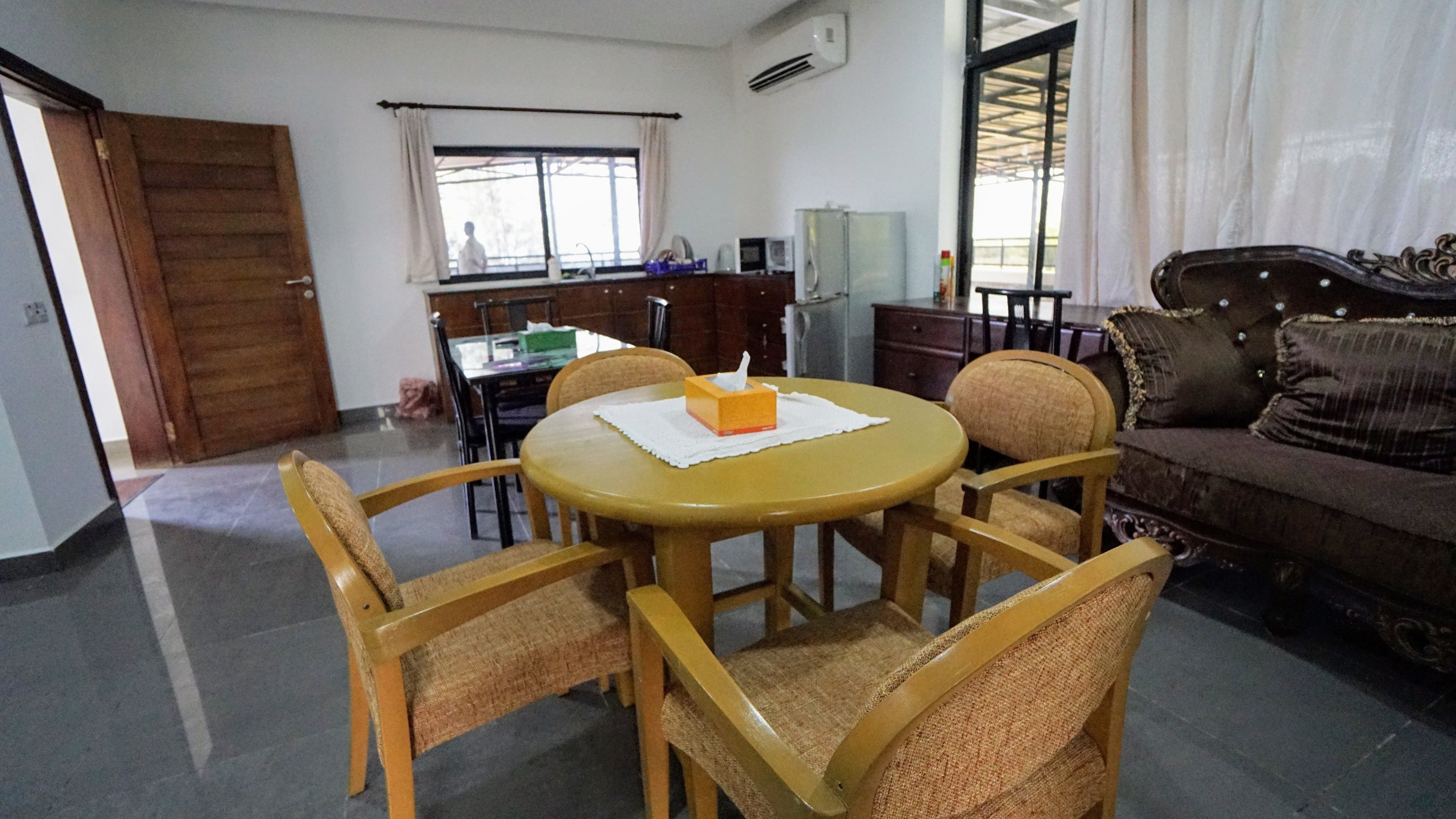 A dining area with a round table, four chairs, a tissue box, and a window with curtains.