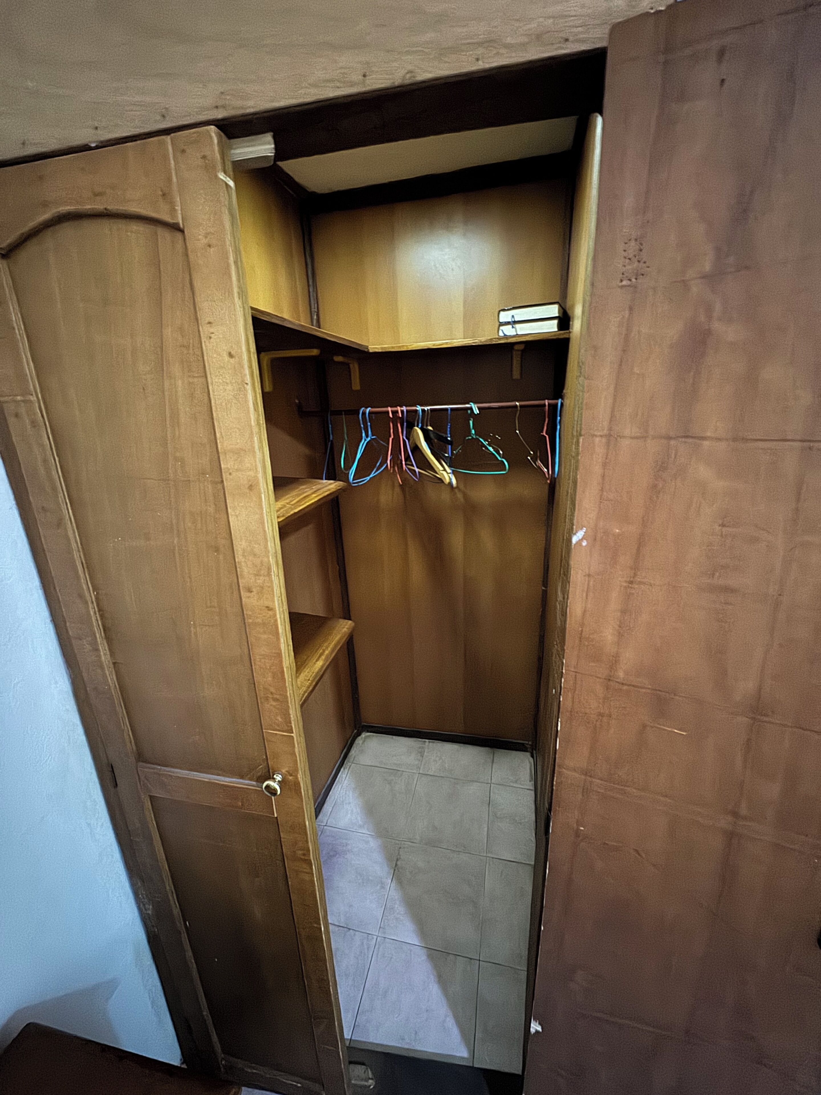 A wooden closet with shelves and hanging clothes.
