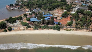 Vista aérea de un pueblo costero con una playa arenosa, edificios de techos azules y palmeras.
