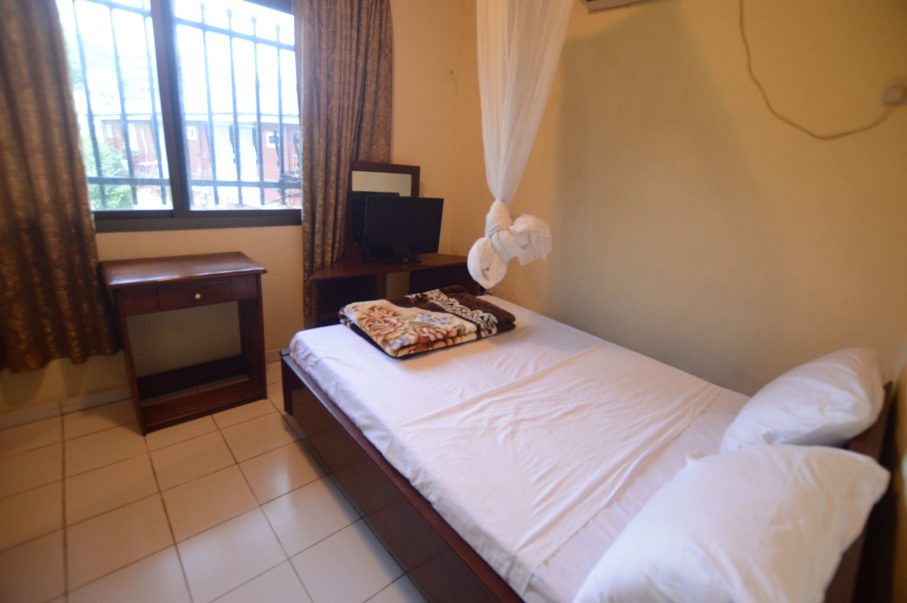 A bedroom with a bed, a desk, a television, and a window with curtains.