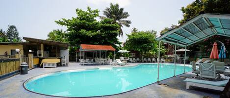 A swimming pool with lounge chairs and umbrellas, surrounded by trees and a covered seating area.