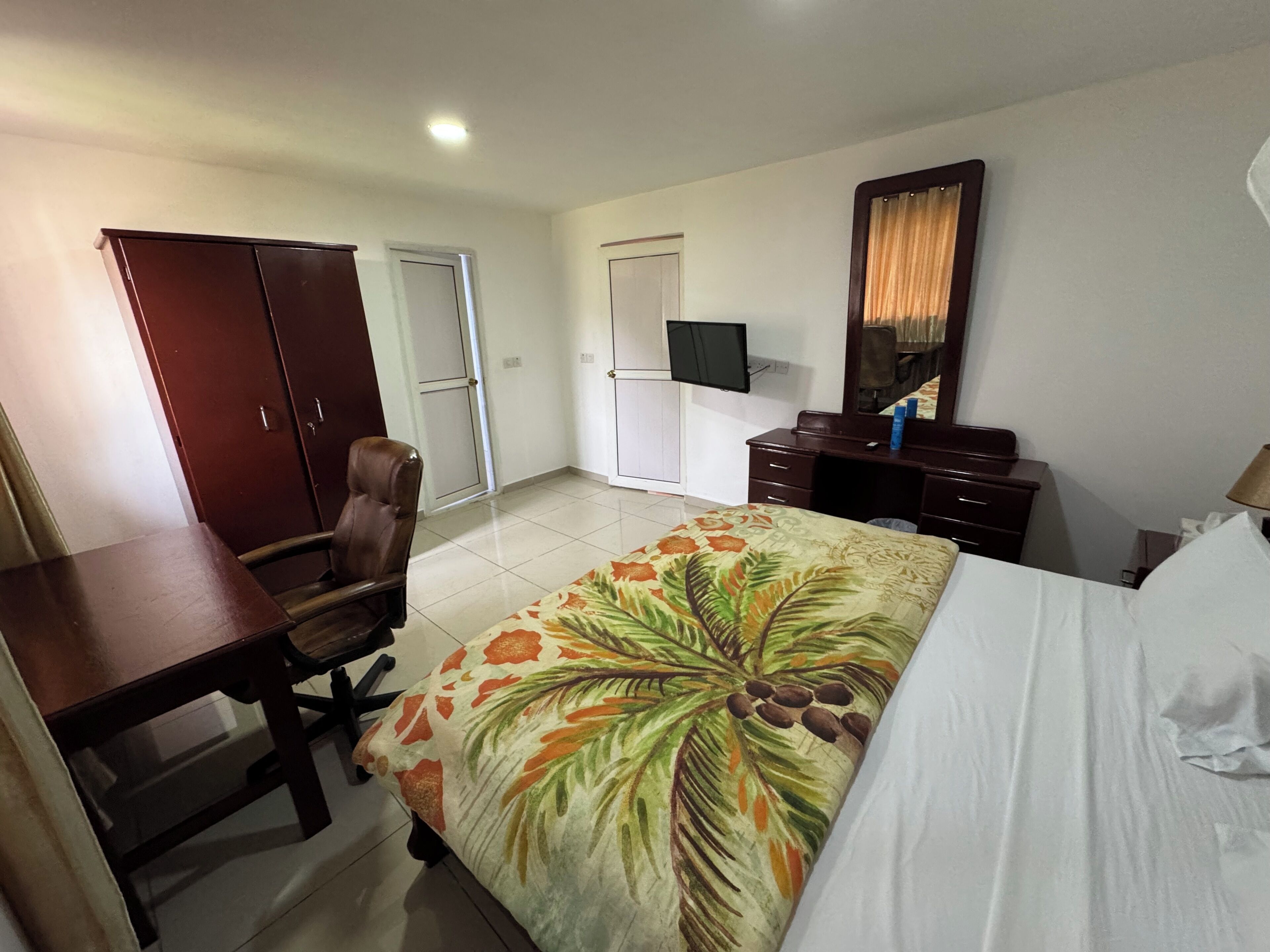 A hotel room with a bed, a desk, a chair, a wardrobe, a television, and a mirror.