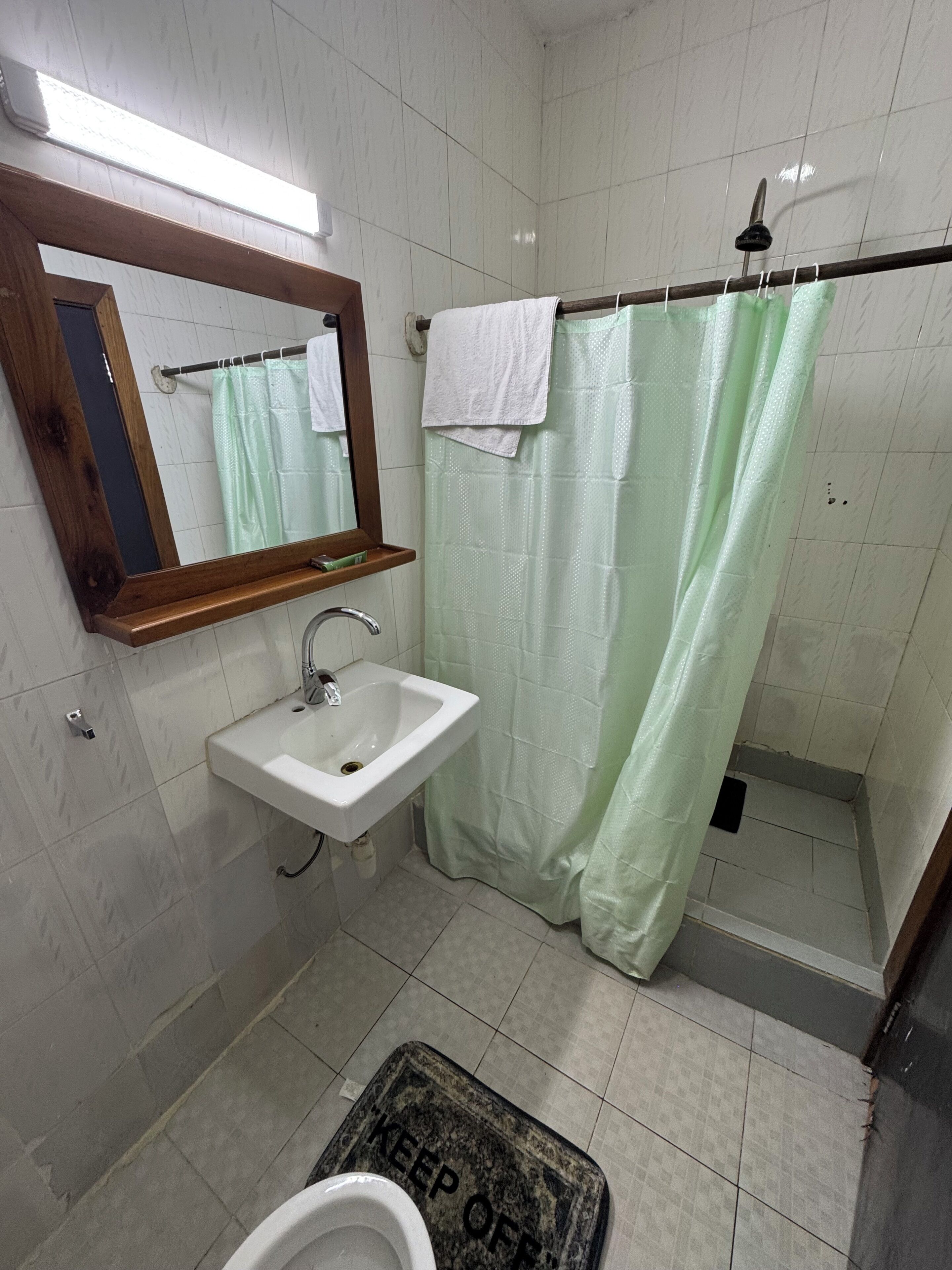 A bathroom with a sink, mirror, shower curtain, and a 'KEEP OFF' mat.