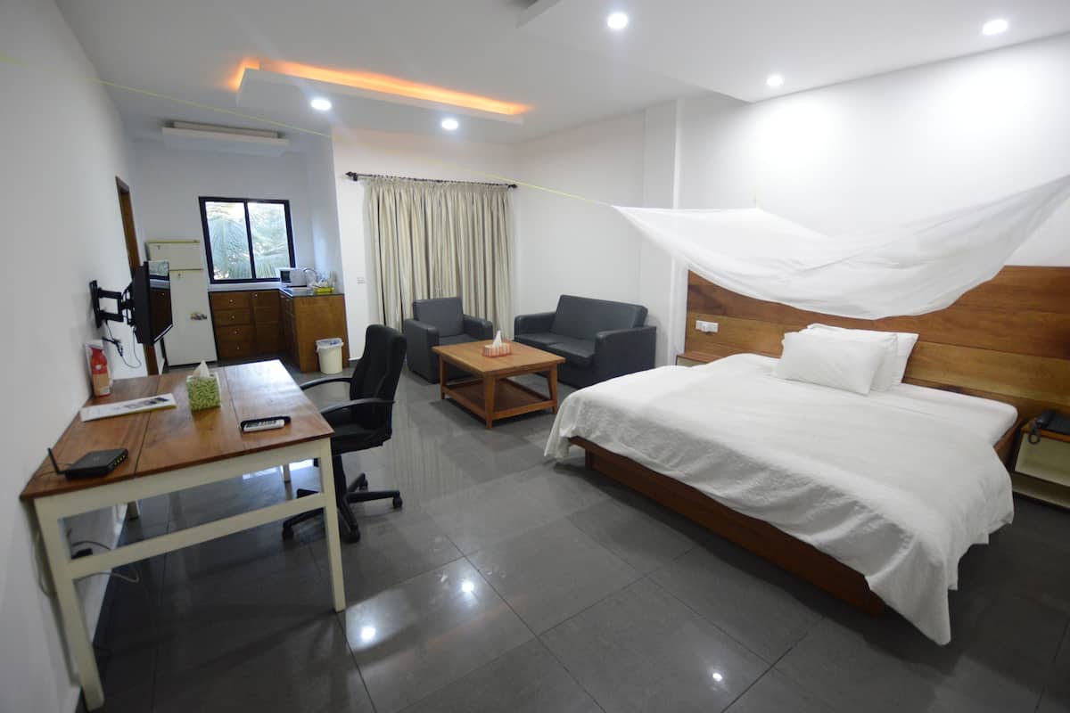 A hotel room with a bed, a desk, a chair, a small table, a TV, and a window.