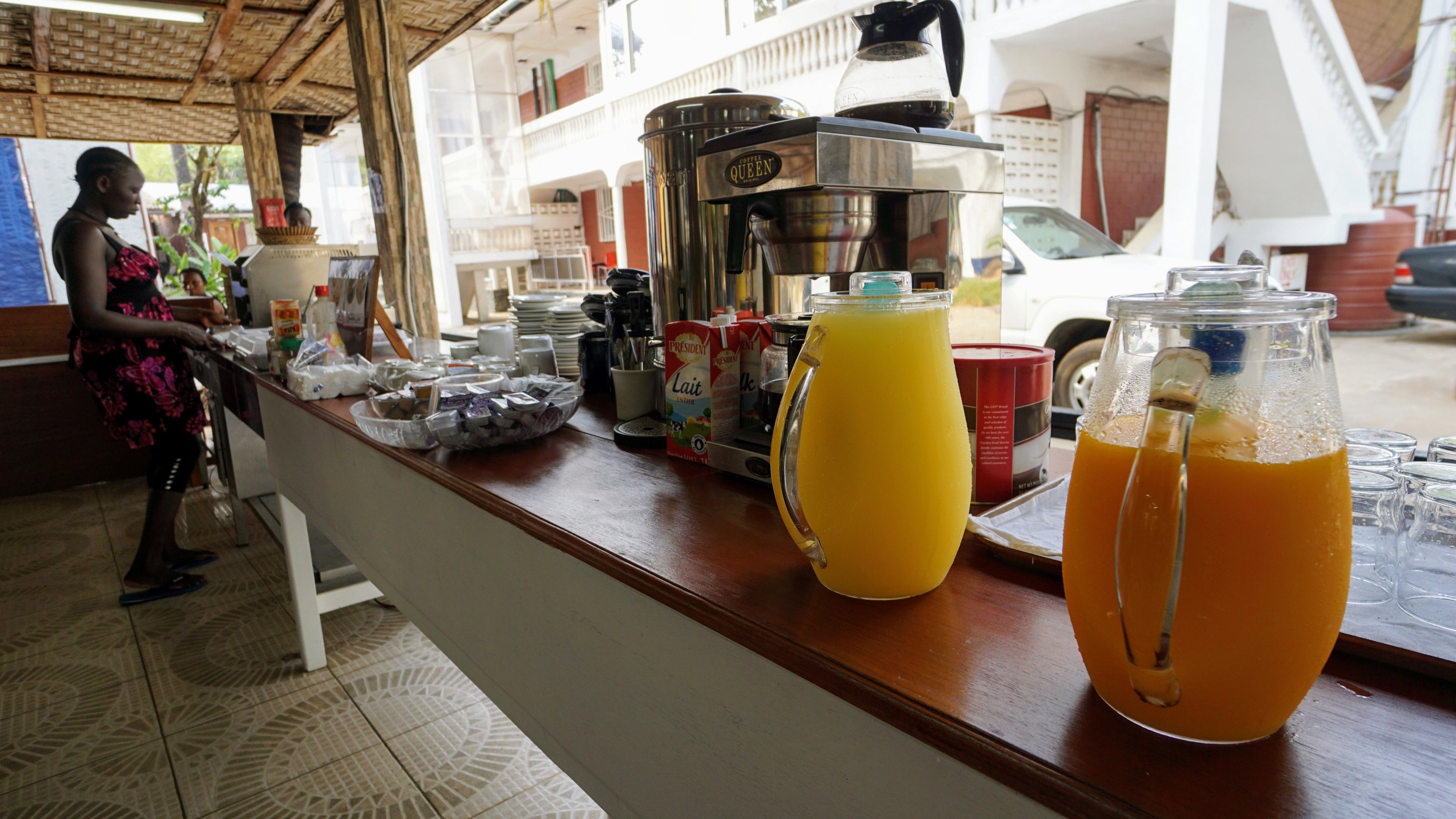 Uma área de bar com uma máquina de café, dispensadores de suco e um balcão com diversos itens.