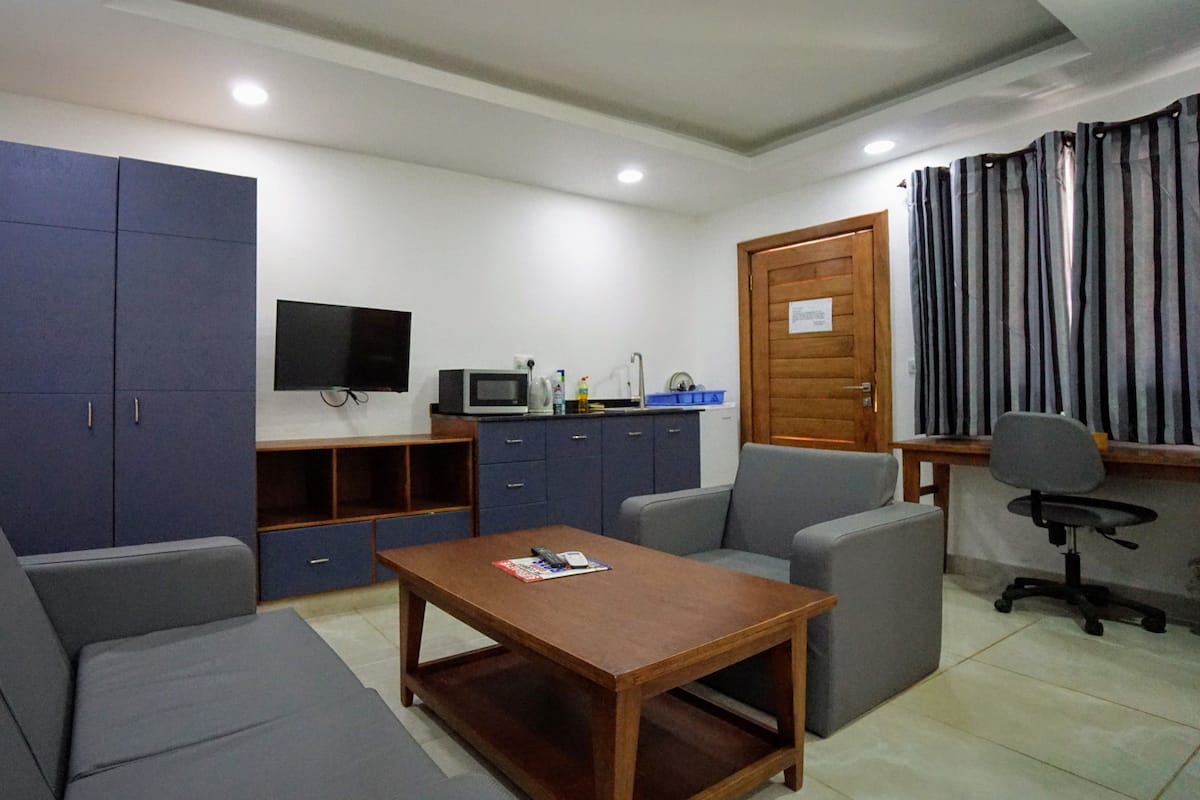 A compact living space with a sofa, a small table, a TV, a kitchenette, and a door with a sign.