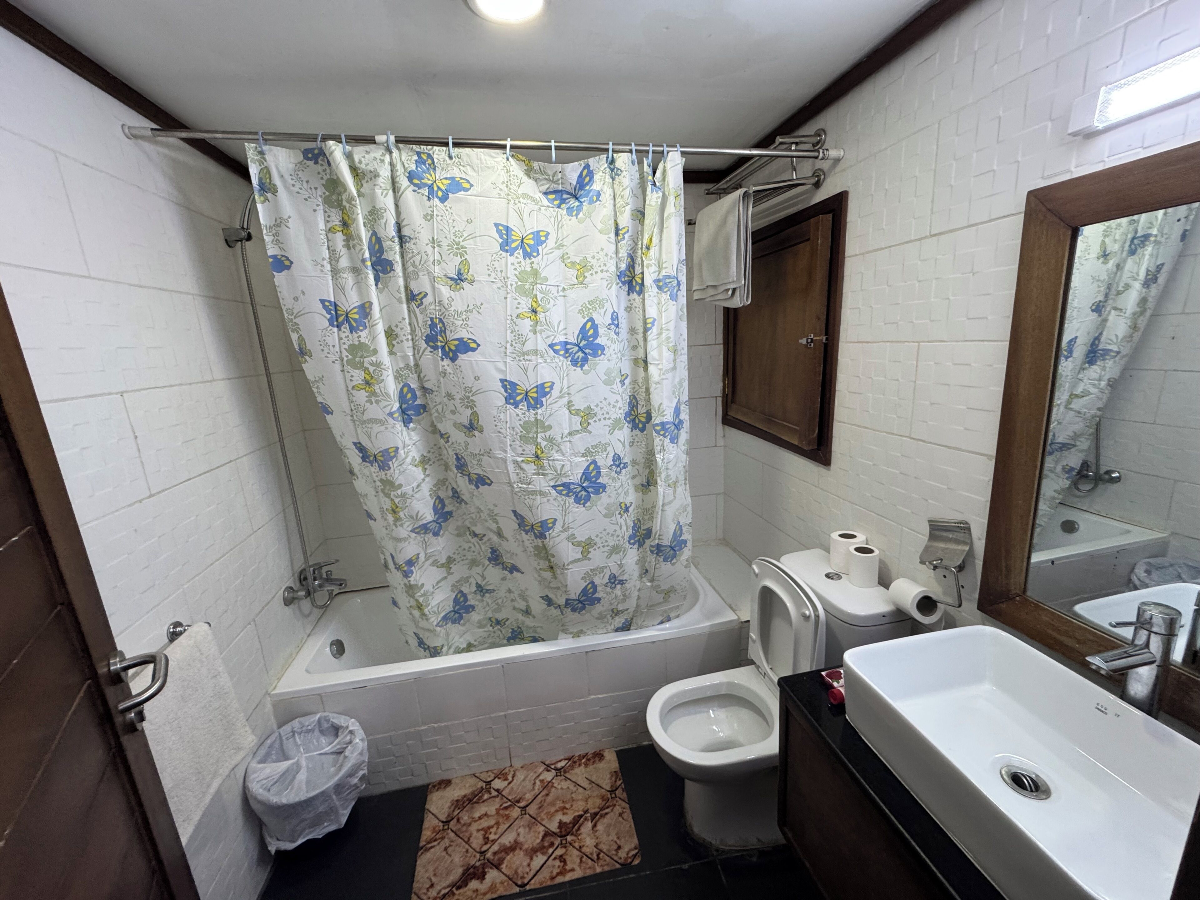 Een badkamer met douchegordijn, toilet, bidet, wastafel en spiegel.