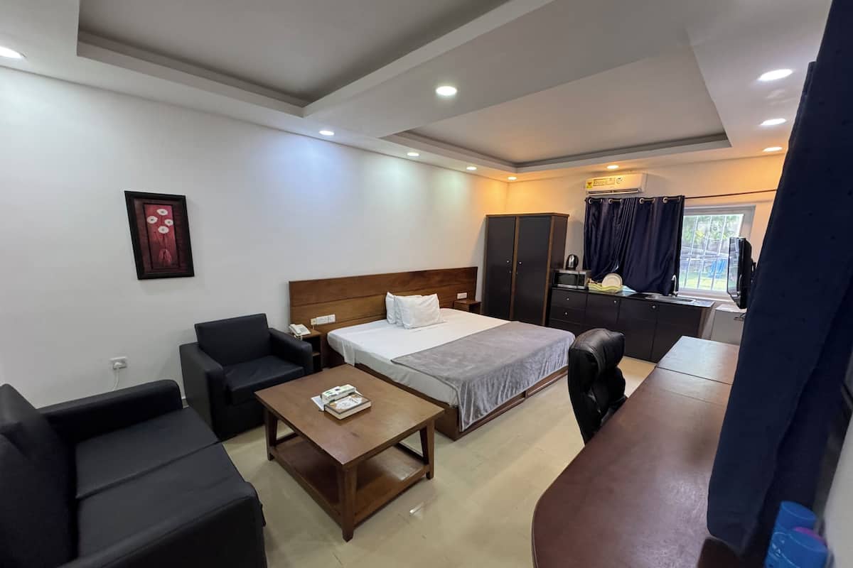 A hotel room with a bed, a sofa, a coffee table, a desk, a wardrobe, and a window with curtains.