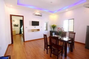 A dining area with a wooden table and chairs, a flat-screen TV mounted on the wall, and an air conditioning unit above the table. - DaNa Home Hotel - Apartment (Da Nang)