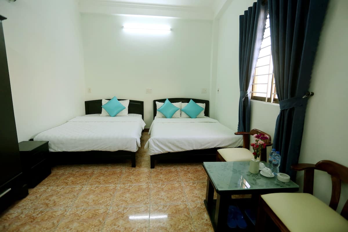 Une chambre d’hôtel avec deux lits, une petite table, une chaise, un téléviseur et une fenêtre avec des rideaux.