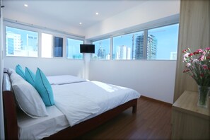 A modern bedroom with a large bed, a flat-screen TV mounted on the wall, and a view of city buildings through large windows. - DaNa Home Hotel - Apartment (Da Nang)