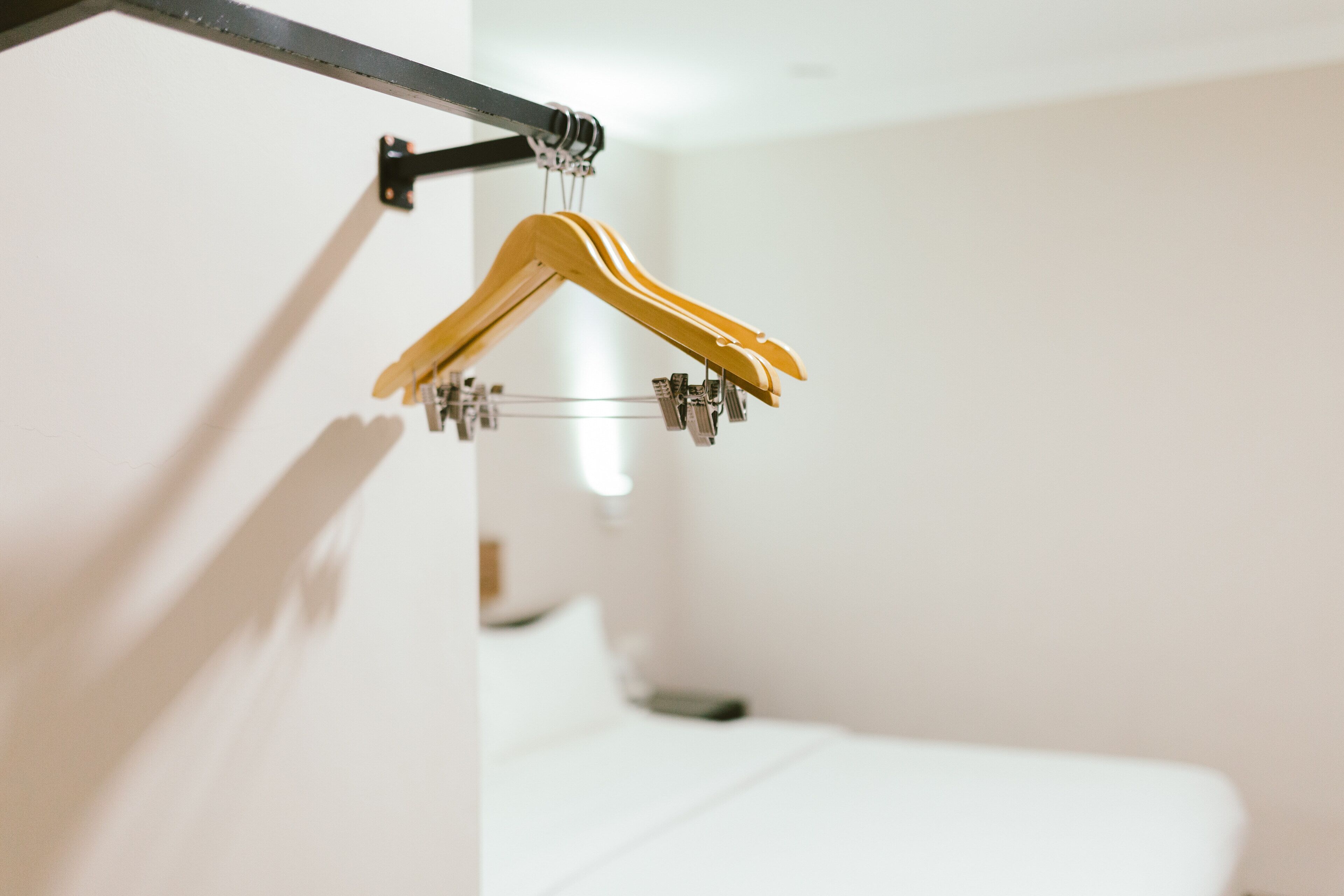 Quarto com uma cama, um porta-roupas fixado na parede com dois cabides amarelos e uma peça de metal.