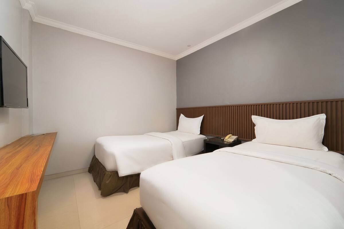 A hotel room with two single beds, a wooden desk, a flat-screen TV, and a wooden headboard.