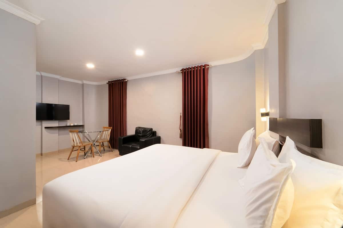 A hotel room with a bed, a TV, a desk with a chair, and a coat rack.
