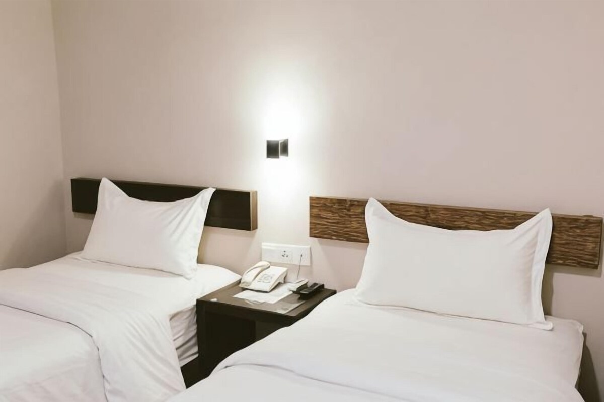 A hotel room with two beds, a bedside table with a phone, and a wall-mounted light.