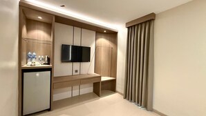 Una habitación de hotel moderna con televisión de pantalla plana en la pared, una pequeña kitchenette con refrigerador y una zona de estar con un banco.